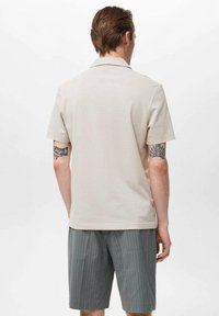 Beige kortärmad skjorta i ett mjukt tyg, med en klassisk krage och en avslappnad passform. Bärs med grå randiga shorts.