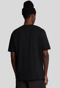 T-shirt nera in cotone con maniche corte, collo a giro e orlo dritto. Indossata con un berretto di lana nero.