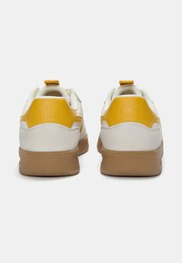 Weiße und gelbe Sneaker verfügen über ein glattes Lederoberteil, eine strukturierten Gummisohle sowie einen markanten gelben Akzent an der Ferse und am Seitenstreifen.