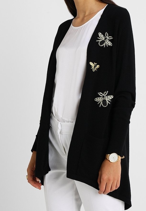 Svart kavaj med tre broderade bi-designs, med avslappnad passform, öppen framsida och två framfickor. Mjuk stickad struktur.