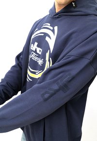 Navyblaues Hoodie mit einem grafischen Aufdruck von "elko Freestyle" in Weiß und Gelb. Enthält eine strukturierte Akzentuierung am Ärmel.