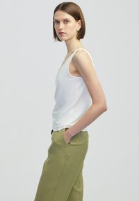 Top bianco senza maniche con una texture liscia, abbinato a pantaloni a gamba larga verde oliva. Il top presenta un design semplice e una forma aderente.