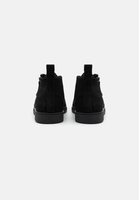 Botines de ante negro con un acabado texturizado, suela de goma plana y dos tiradores verticales en la parte trasera para facilitar su uso.