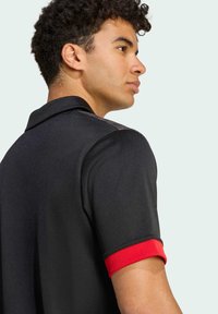 Sort polo-shirt med et ensfarvet design, der har røde manchetter og en detaljeret krave. Stoffet ser glat ud med en let glans.