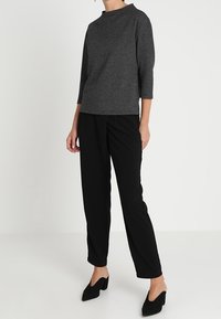 Top gris de manga tres cuartos con un cuello alto, combinado con pantalones rectos negros y tacones negros. Textura de tela suave, diseño minimalista.