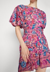 Vestido corto floral en rosa, con mangas abullonadas, cintura ceñida con un cinturón, y un dobladillo con volantes con acentos en azul y morado.