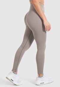 Beige geribbelde leggings met hoge taille, een soepele textuur en versterkte stiksels, gecombineerd met een witte sneaker met zichtbare luchtvering.