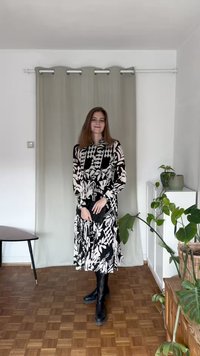 Vestido de manga longa preto e branco com padrões de folhas e geométricos, botões na frente, combinado com botas pretas até ao joelho.