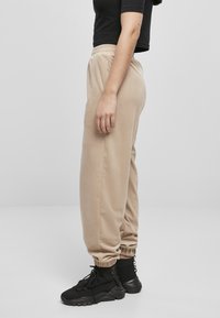 Beige joggerbyxor gjorda av mjukt material, med ett elastiskt midjeband och mudd i fotleden. Kombineras med svarta högstövlar för kontrast.