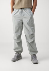 Light gray, lightweight trousers with an elastic waistband, side pockets, and a relaxed fit. Material appears smooth with a subtle sheen.