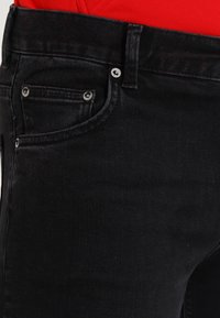 Černé džíny z denimu s klasickým pětipocket designem, viditelným šitím a stříbrnými kovovými detaily na předních kapsách.