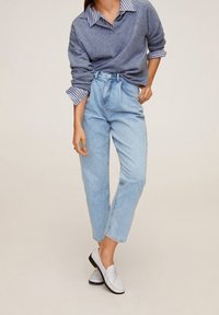 Jasnoniebieskie dżinsy z wysokim stanem zestawione z szarym swetrem na paskowanej koszuli z kołnierzykiem, uzupełnione białymi mokasynami.