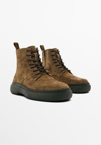 Bottines en suède marron avec lacets noirs, semelle sombre rembourrée et tirants à l'arrière pour un enfilage facile. Texture lisse et design classique.