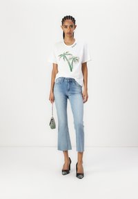 T-shirt bianca con design di palme in verde e decorazioni in argento, jeans blu a vita alta e taglio cropped, e décolleté nere con dettagli lucidi.