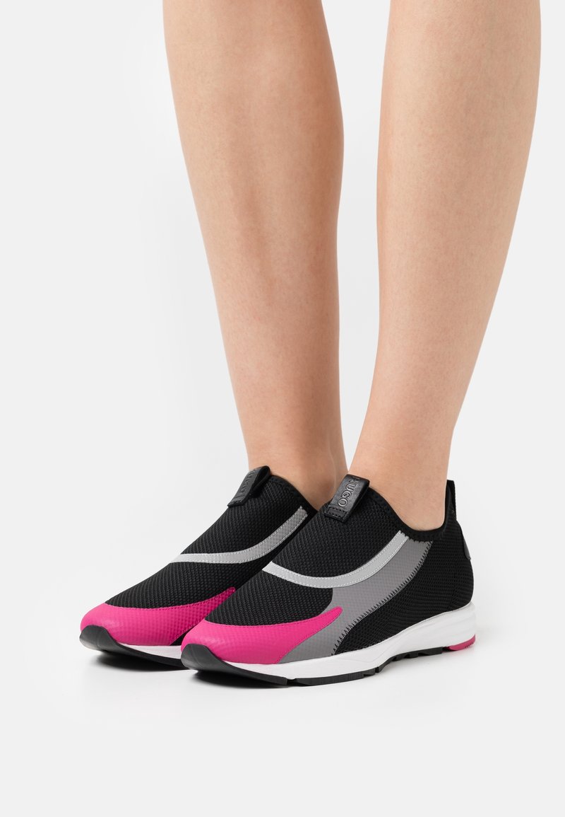 Černé sportovní slip-on boty s síťovým svrškem, se zvýrazněním v růžové a šedé barvě, texturovaným povrchem a lehkou bílou podrážkou.