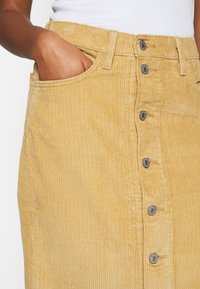 Gul kordoroy midi kjol med knäppning fram, fem knappar och sidofickor med vertikalt ribbad textur.