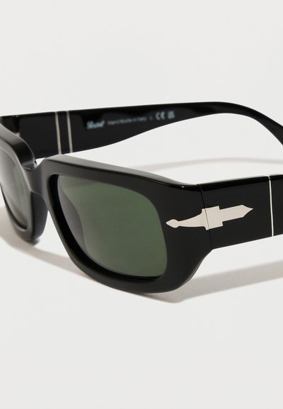 Óculos de sol pretos com lentes grandes, tonais verdes e uma textura brilhante. Apresentam um detalhe em metal prateado na haste com um elemento de design pontiagudo.