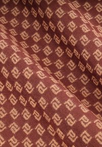 Woven textile with a rich burgundy background and a geometric tan pattern of squares and diamonds, featuring a soft, textured surface.