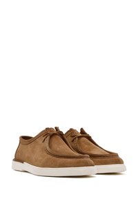 Chaussures en daim marron à design à tige basse, bout rond et semelle en caoutchouc blanc. Présentent des lacets décoratifs et une texture lisse.