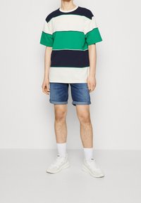 T-shirt rayé en marine, vert et blanc, associé à un short en denim clair. Des baskets blanches complètent la tenue. Design et coupe décontractés.