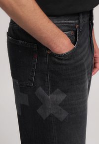 Jeans in denim neri con una finitura sbiadita, caratterizzati da un sottile motivo a incrocio sulla coscia, design a cinque tasche e dettagli in ottone.