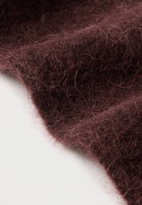 Tecido bordô entrelaçado com uma textura macia e felpuda, apresentando fibras soltas e uma borda ligeiramente irregular.