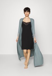 Robe lungo e aperto davanti di un teal chiaro con dettagli in pizzo ai polsini, indossato sopra un vestito sottoveste nero con scollo in pizzo.