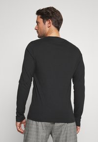 Cămașă neagră cu mânecă lungă, fabricată dintr-un material moale, cu decolteu rotund și o formă ajustată, având o textură netedă și elemente de design minimale.