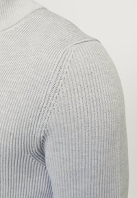 Suéter de canalé gris claro con cuello alto, tela texturada y silueta ajustada, que enfatiza las rayas verticales y la durabilidad.