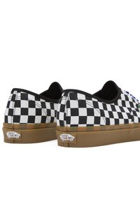 Black and white checkerboard canvas shoes with a low-profile design, gum rubber sole, and Vans logo on the heel, featuring blue accents.