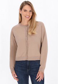 Vaatettu beige neulecardigan, jossa on pyöreä kaula-aukko, napitus, ribbireunukset hihansuissa ja helmassa. Yhdistetty tummansinisiin farkkuihin. Suora pinta, vartalonmyötäinen muotoilu.