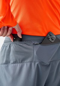 Mäns sportshorts i mörkgrått med en texturerad yta, med en zipficka. En orange långärmad tröja syns ovanför midjebandet.