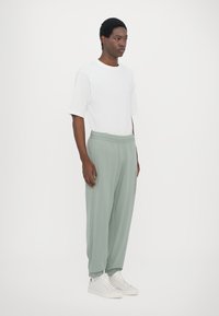 Bijela majica i zelene hlače s elastičnim pojasom i manžetama, uparene s bijelim tenisicama. Kombinacija ima opušteni kroj i glatku teksturu.