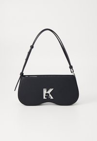 Borsa nera con una forma curva, materiale testurizzato, logo argentato e una tracolla sottile. Chiusura superiore con cerniera e caratteristiche di design minimalista.