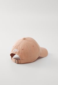 Pale rózsaszín, puha anyagú baseball sapka, ívelt karimával, fehér Nike logóval hímezve az oldalon, hátul állítható fémszíjjal.