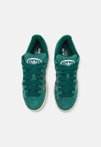 Grüne Wildledersneaker mit strukturierten Schnürsenkeln, abgerundetem Zehenbereich und weißen Logoakzenten. Verfügt über drei seitliche Streifen in einem etwas dunkleren Farbton.