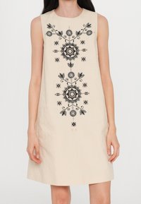 Vestido sin mangas de color beige con intrincados bordados florales negros en la parte frontal, escote redondo y silueta recta.