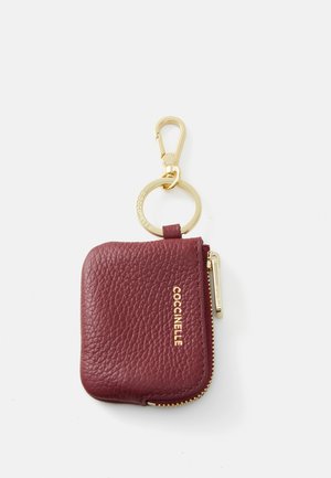 Burgundy leather keychain wallet with a gold zipper, keyring, and clip. Textured finish with a gold logo embossed on the front.