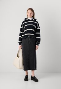 Felpa a strisce blu navy e bianca con logo frontale, abbinata a una lunga gonna di jeans nera, mocassini neri con piattaforma e una borsa a tracolla beige chiaro.