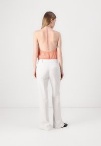 Takab back is a person who is wearing an orange, sparkly halter top which is paired with white, high-waisted, flared trousers and black slip-on shoes.