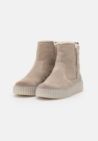 Botines de ante beige con un interior acolchado, cremalleras laterales y una suela de caucho blanca texturizada.