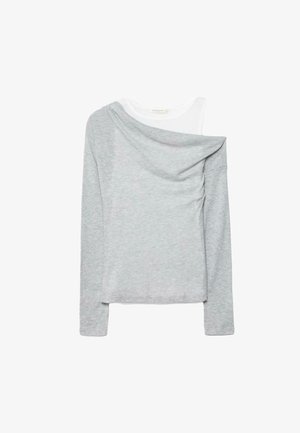 Svetlo siva majica z dolgimi rokavi, ki je oblečena čez belo majico brez rokavov, sivo majico pa je asimetrično oprta na enobarvnem belem ozadju.