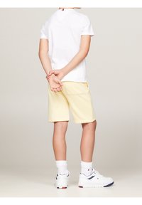 Witte T-shirt met korte mouwen, gecombineerd met gele shorts met zijzakken. De outfit wordt afgewerkt met witte sneakers en crew-sokken.