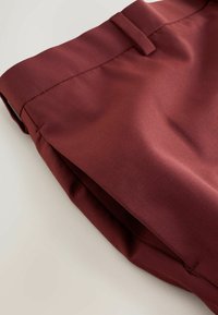 Bordeauxfarbene Stoffshorts mit glatter Textur, versehen mit einem gefalteten Bund und scharfen Falten an den Beinen. Sauberes, einfaches Design ohne Muster.