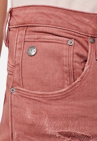 Shorts de mezclilla rosa desgastados con un bolsillo delantero, herrajes plateados y detalles desgastados en la tela.