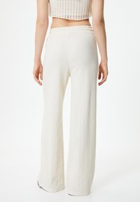 Pantalons larges en tissu texturé crème avec une taille élastique. Le design présente une surface douce et fripée ainsi qu'une coupe polyvalente.