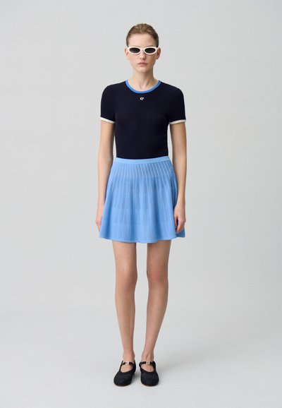 Top de manga corta de canalé en color navy con acentos en azul claro, combinado con una minifalda plisada en azul claro. Zapatos negros trenzados y gafas de sol blancas.