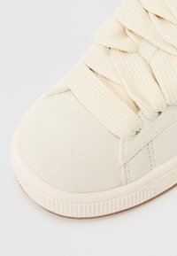 Kreminių zomšinų sportbačiai su storomis kreminėmis nėrėmis, apvaliu pirštu, tekstūruotu paviršiumi ir kontrastinga guma, turinčia įstrukturinį dizainą.