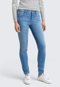 Vaqueros skinny de un azul claro en denim con una cintura de altura media, dos bolsillos frontales y un ligero desgastado. Combinados con zapatillas blancas y una blusa de rayas.