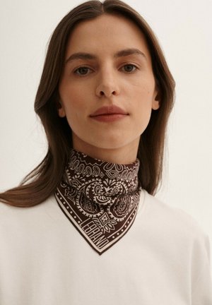 Brązowa, wzorzysta chusta w stylu bandany z tkaniny, złożona z misternych wzorów i w kształcie trójkąta, noszona wokół szyi modelki.